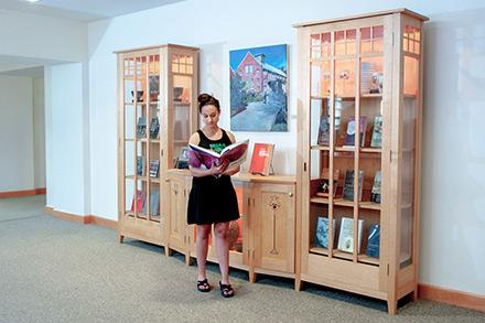 A person reading in front of a case of faculty books