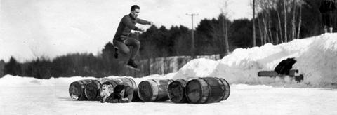 student outdoors in the winter jumping over barrels on ice skates 