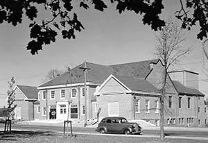 New Hampshire Hall with people clustered outside of entrance and car parked in front.