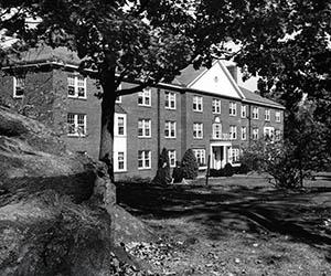Front of Sawyer Hall with trees and large rock in the foreground.