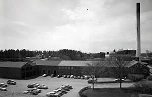 Service building with cars in foreground and smokestack in background.