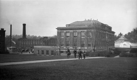 Men walking on a sidewalk between DeMeritt Hall and Thompson Hall in 1924