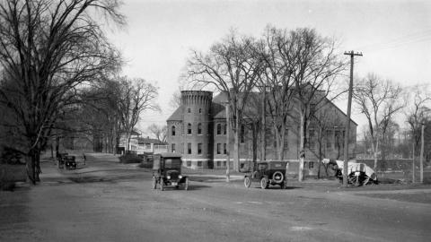 The Armory-Gymnasium with a turret and some old fashioned cars along the old packed dirt street